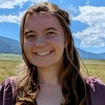 A headshot of Stella Corgan a white woman in a purple shirt and brown hair smiling at the camera.
