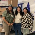 The Interfaith Works Essential Needs Center Team consisting of 3 black women standing together and smiling for the camera. One is in a green hat and green CK shirt, the woman in the middle is in a white t-shirt and blue jeans and the last lady is in a black and white shirts and light blue jeans.
