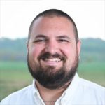 A headshot of Sam Havighurst, the Executive Director of North Carroll Community School. Sam is shown with a shaved head, beard and big smile.
